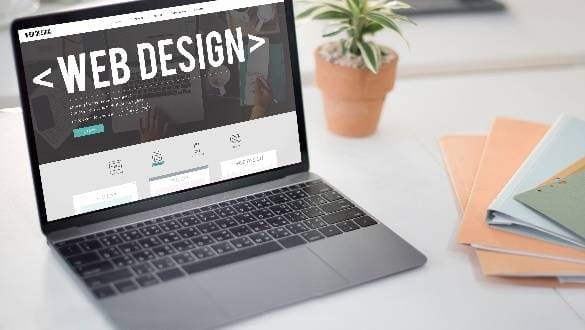 Laptop displaying web design content on a desk with a plant.
