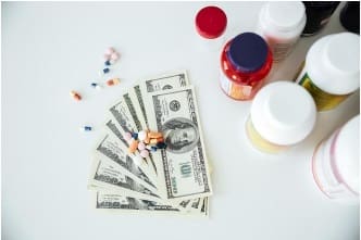 Pills and medicine bottles on top of several US dollar bills.