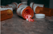 Orange pill bottles spilled with pink heart-shaped pills on a surface.