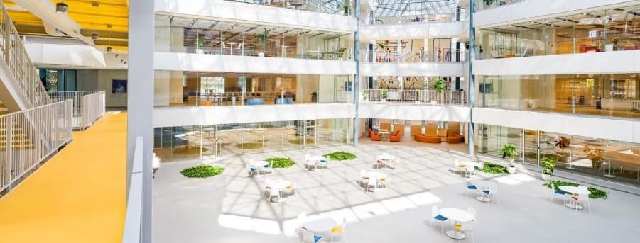 Bright modern atrium with sunlight, plants, and seating areas.