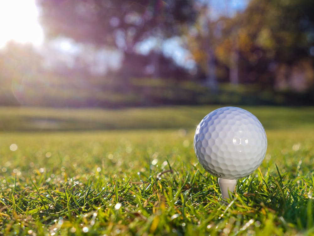 Golf ball on tee with sunlit fairway