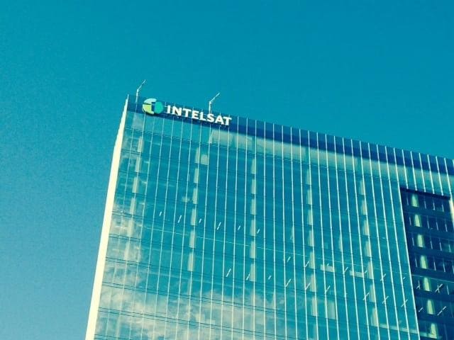 Tall modern glass building with IntelSat logo against clear sky.