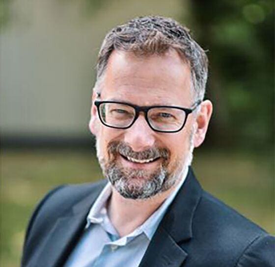 A smiling man with glasses and a beard wearing a suit jacket.