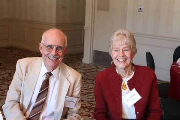 Two elderly individuals smiling at a formal event.