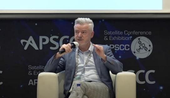 A man speaking at a conference, holding a microphone.