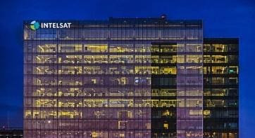 Illuminated modern office building at night with many windows and the word SAT on top.