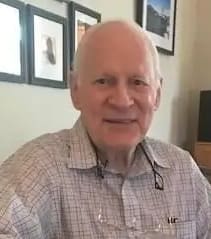 Smiling elderly man in a casual plaid shirt indoors.