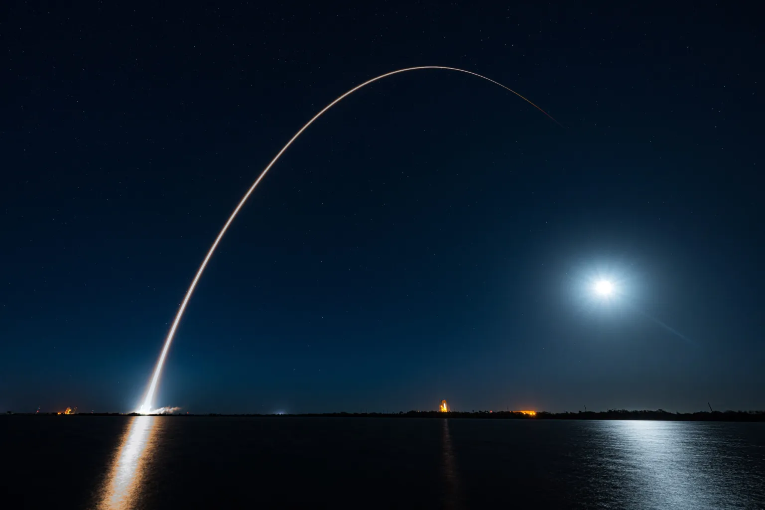 A missile launching into the night sky over water.