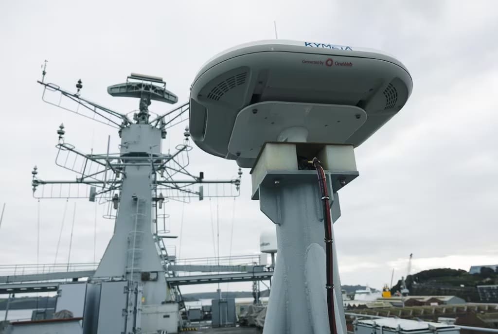 Radar and communication equipment on a naval ship's mast under cloudy sky.