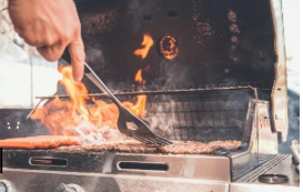 Hand flipping burgers over open grill flames
