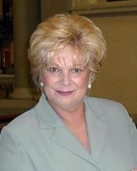 Smiling older woman with short blonde hair and light blue blazer.