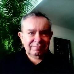 Portrait of a smiling elderly man indoors with greenery in the background.