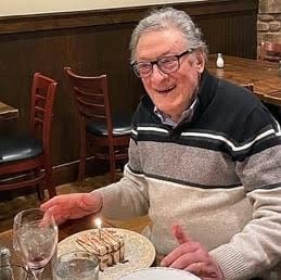 Elderly man smiling at a restaurant table with dessert.