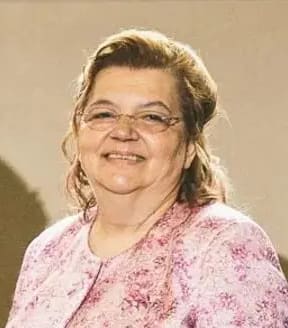 Smiling elderly woman wearing glasses and a pink floral blouse.