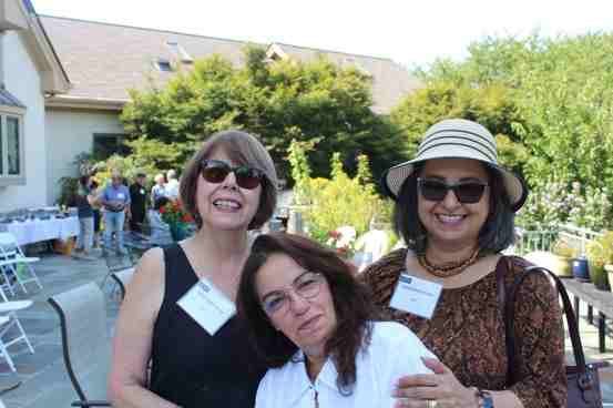 Three women smiling outdoors at a social event on a sunny day.