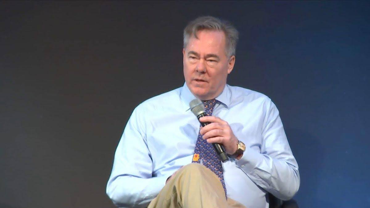 Man in a light blue shirt speaking into a microphone.