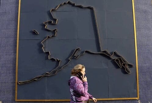 Woman walking past a large outline map on a dark wall.
