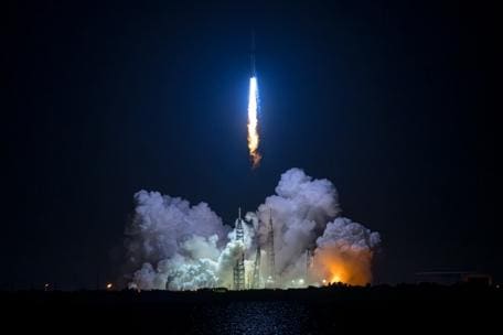 Rocket launching into the night sky with smoke and fire below.