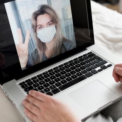Person video chatting on laptop, showing peace sign.