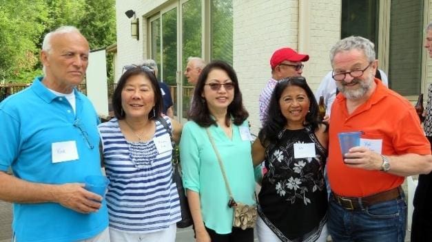 Three women smiling outdoors, dressed casually with sunglasses and bags.