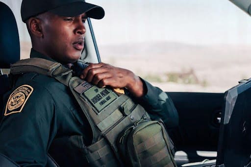A man in tactical gear sitting inside a vehicle, looking focused.