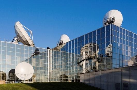 Modern building with satellite dishes on the roof under a clear blue sky.