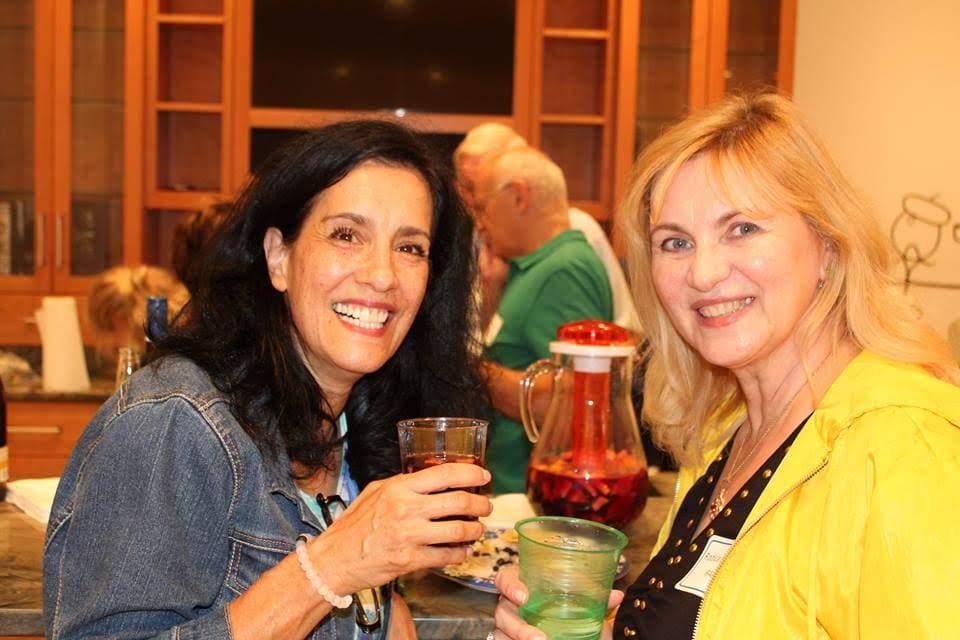 Two women smiling and holding drinks in a cozy setting.
