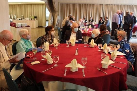 People gathered around a table at a formal event with red tablecloths.