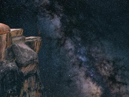 Starry night sky with the Milky Way over rocky cliffs.
