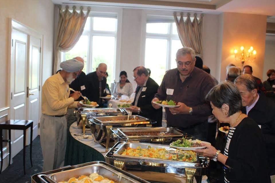 People serving themselves food at a buffet in a well-lit room.