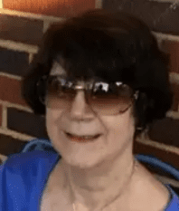Woman wearing sunglasses, smiling near brick wall.