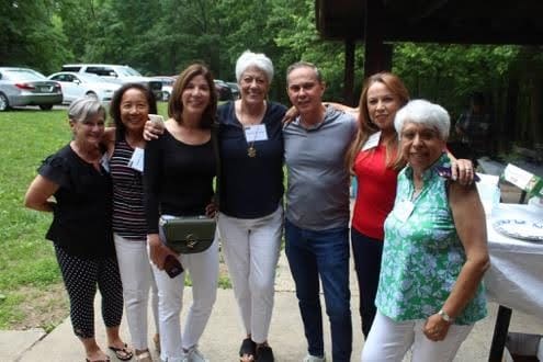 A group of seven people posing outdoors on a sunny day.