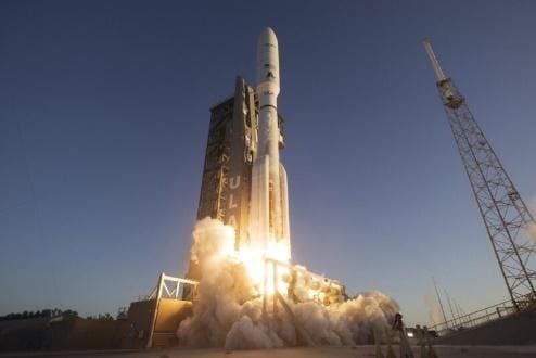 A rocket launching with bright flames and smoke at dusk.