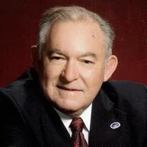 Elderly man in suit with red background.