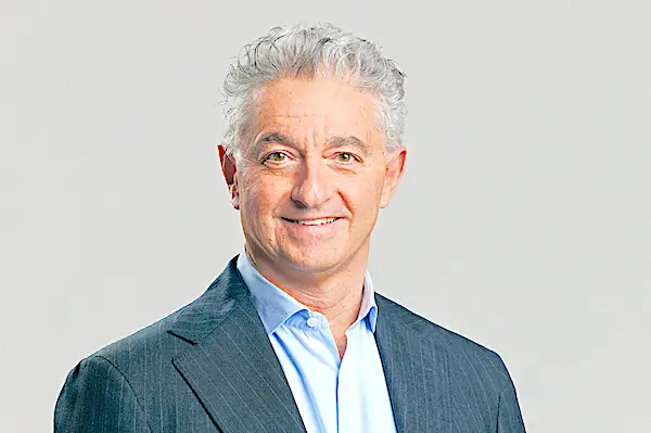 Smiling man in suit, light gray background.