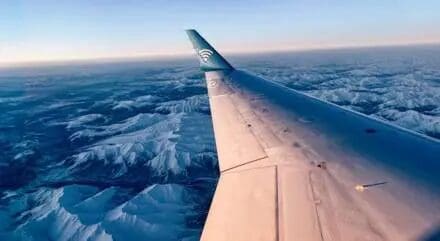 Airplane wing above snowy mountain landscape.