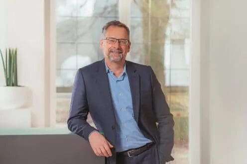 Man in suit smiling by a window.