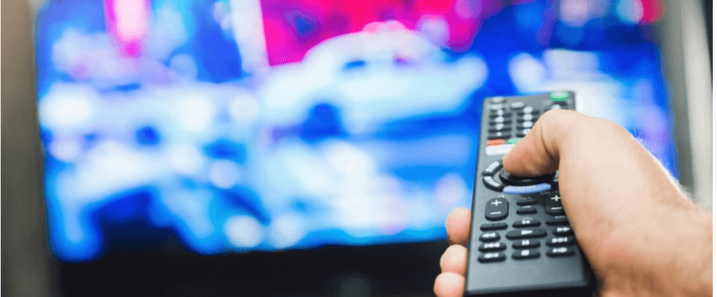 Hand holding remote, pointing at blurred TV.