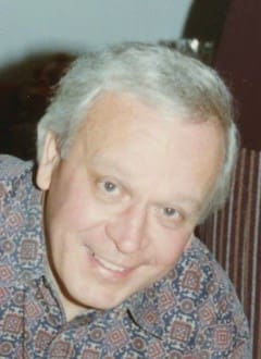 Smiling man with gray hair and patterned shirt.