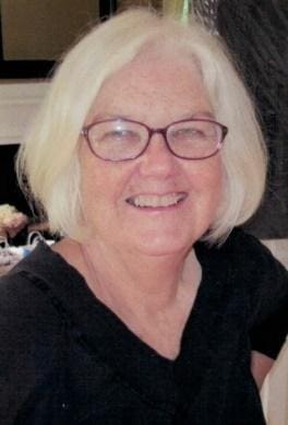 Smiling woman with glasses and white hair.
