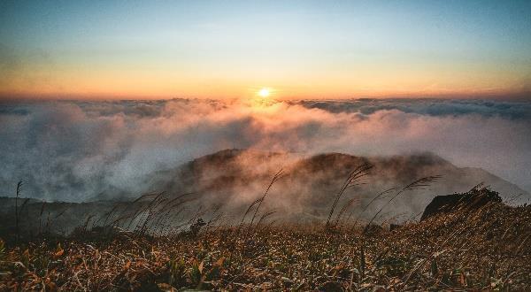 Sunset over misty mountains and grassy hills.