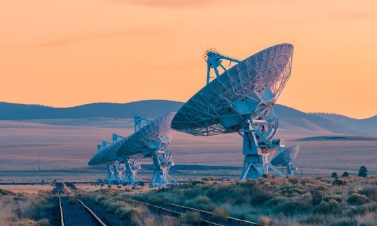Satellite dishes in a desert landscape at sunset.