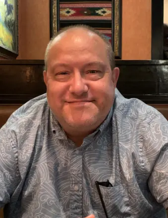 Man smiling in a patterned shirt indoors.