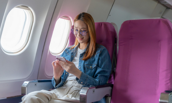 Passenger using phone in airplane window seat.