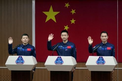 Three astronauts saluting, Chinese flag behind.