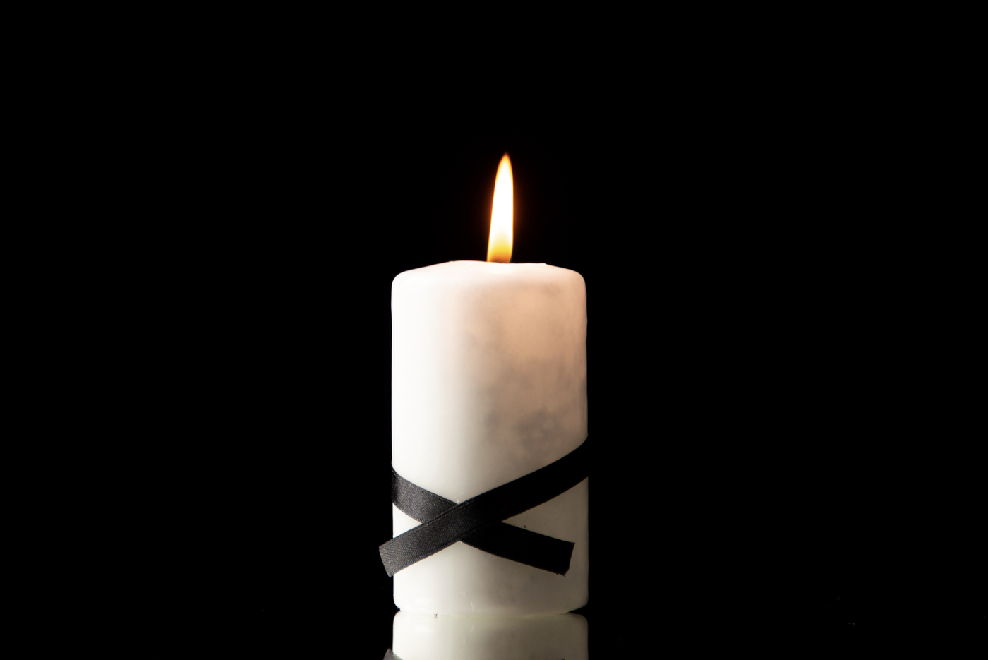 Lit candle with black ribbon on black background.