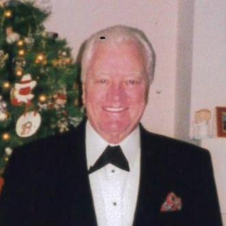 Man in tuxedo smiling by Christmas tree.