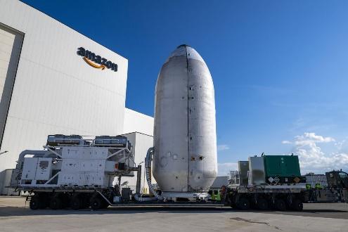 Rocket component on transport vehicle near building.