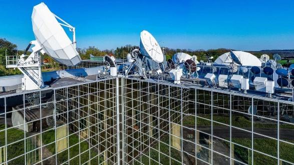 Satellite dishes on a rooftop with fencing.