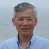 Smiling man in blue shirt by ocean.